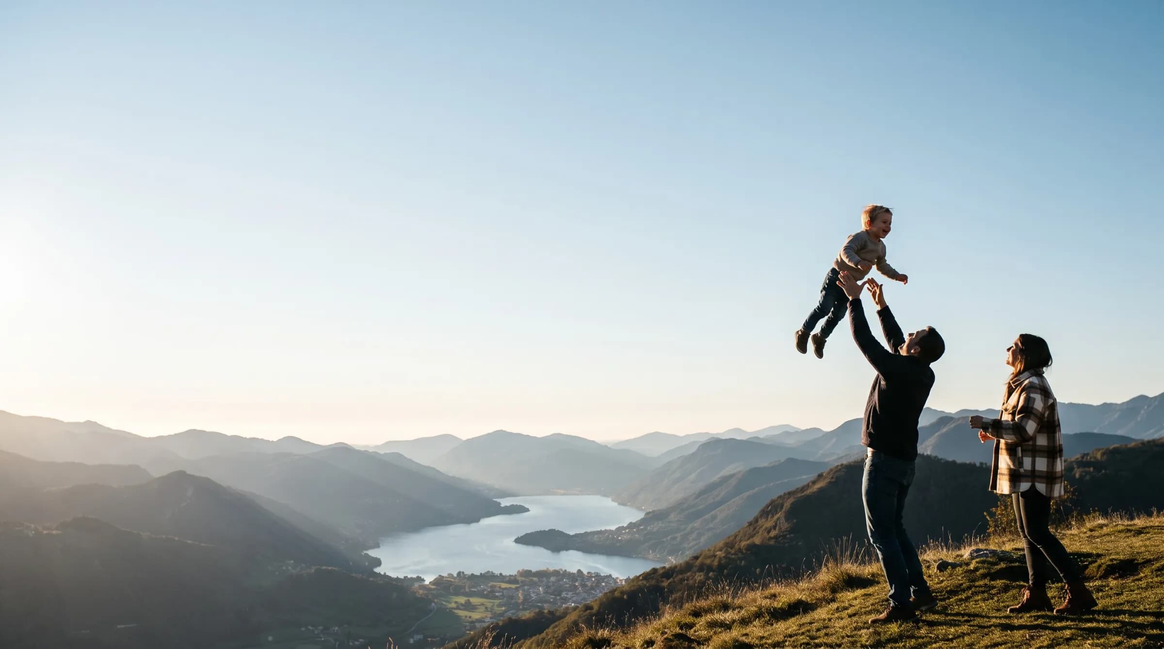 A family on a hilltop at golden hour, a father lifting his child into the air